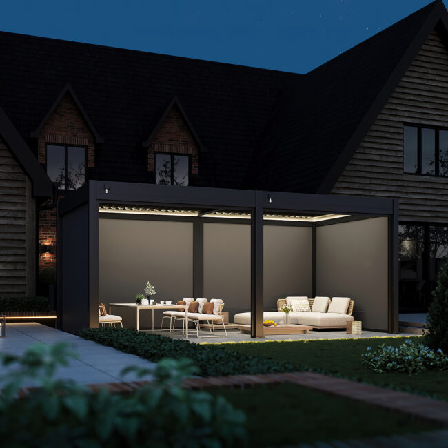 Dark grey pergola with integrated LED ceiling lights and retracted blinds, placed on a paved garden patio with warm underfoot lighting.