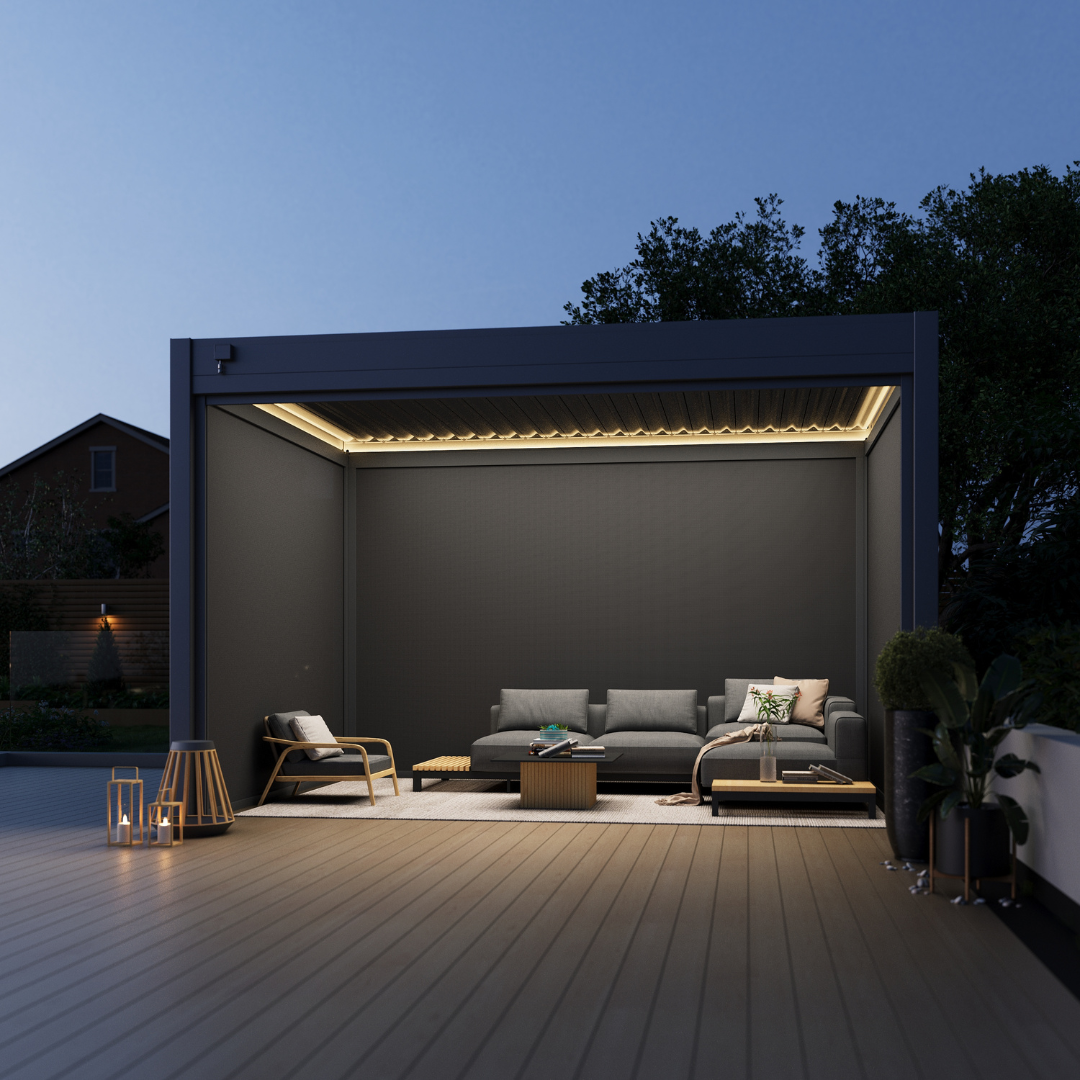 Freestanding pergola with built-in LED beams, located on a wide wooden deck with modern garden sofas, throw pillows, and surrounding shrubbery.