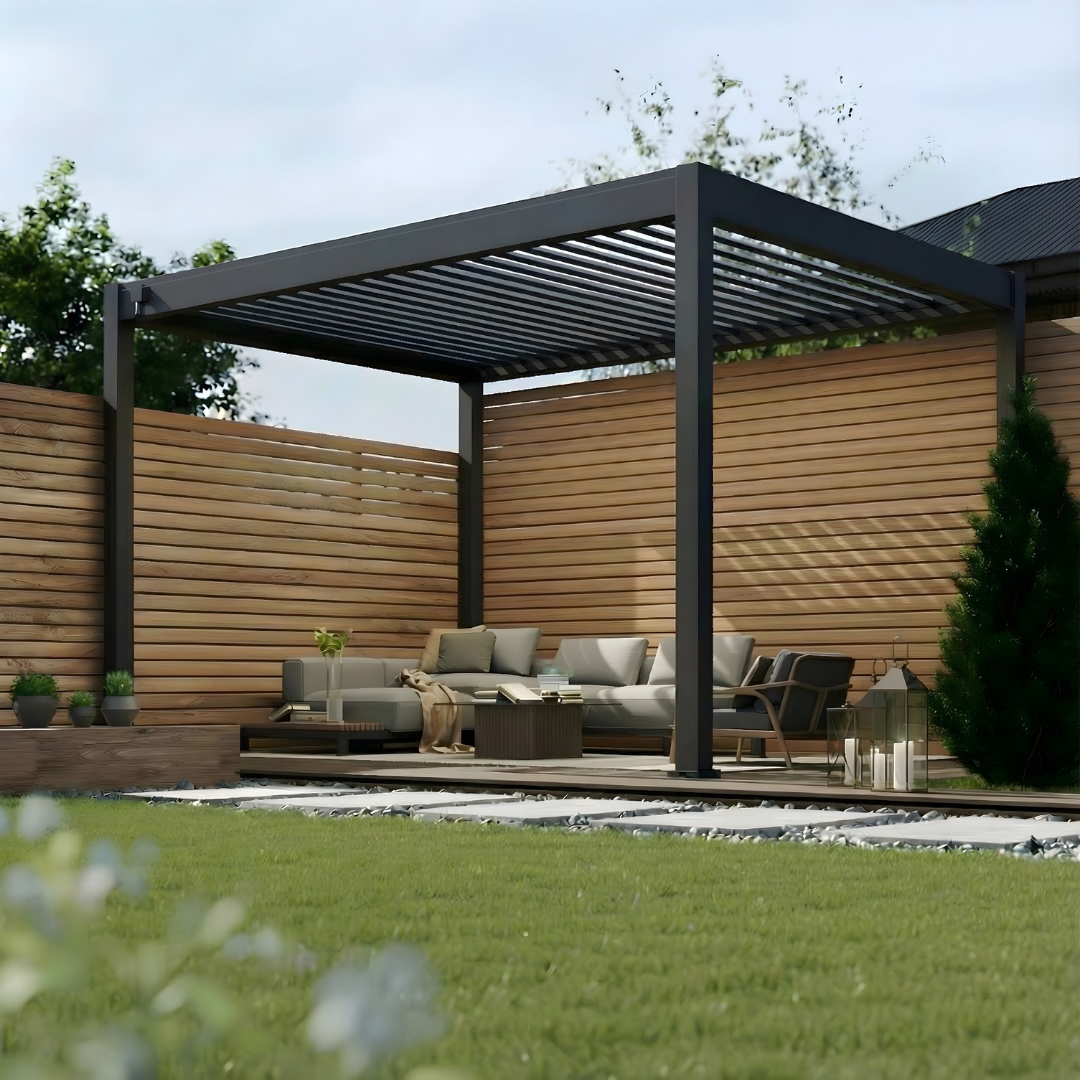 Freestanding dark grey Hygge aluminium pergola with open louvred roof, shown during daytime on a modern deck with natural timber fencing and outdoor lounge seating.