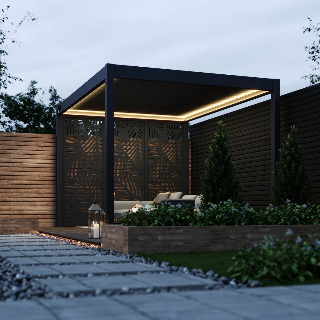 Modern dark grey aluminium pergola with LED strip lighting, set on a gravel patio with landscaped hedging and decorative lighting for a tranquil garden retreat.