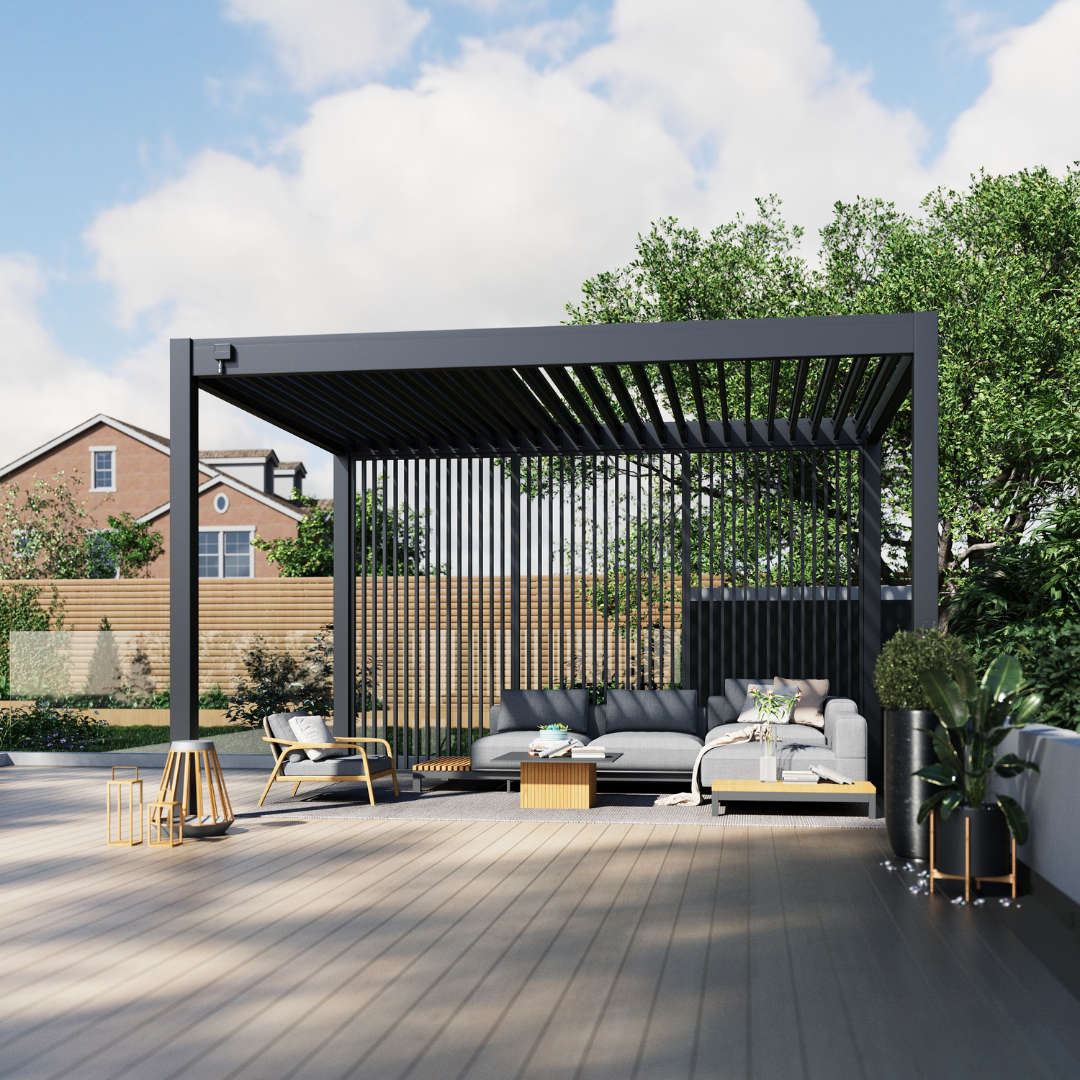 Dark grey pergola with vertical aluminium slats providing semi-privacy, placed on a wide timber deck with woven outdoor chairs, a side table, and potted shrubs.