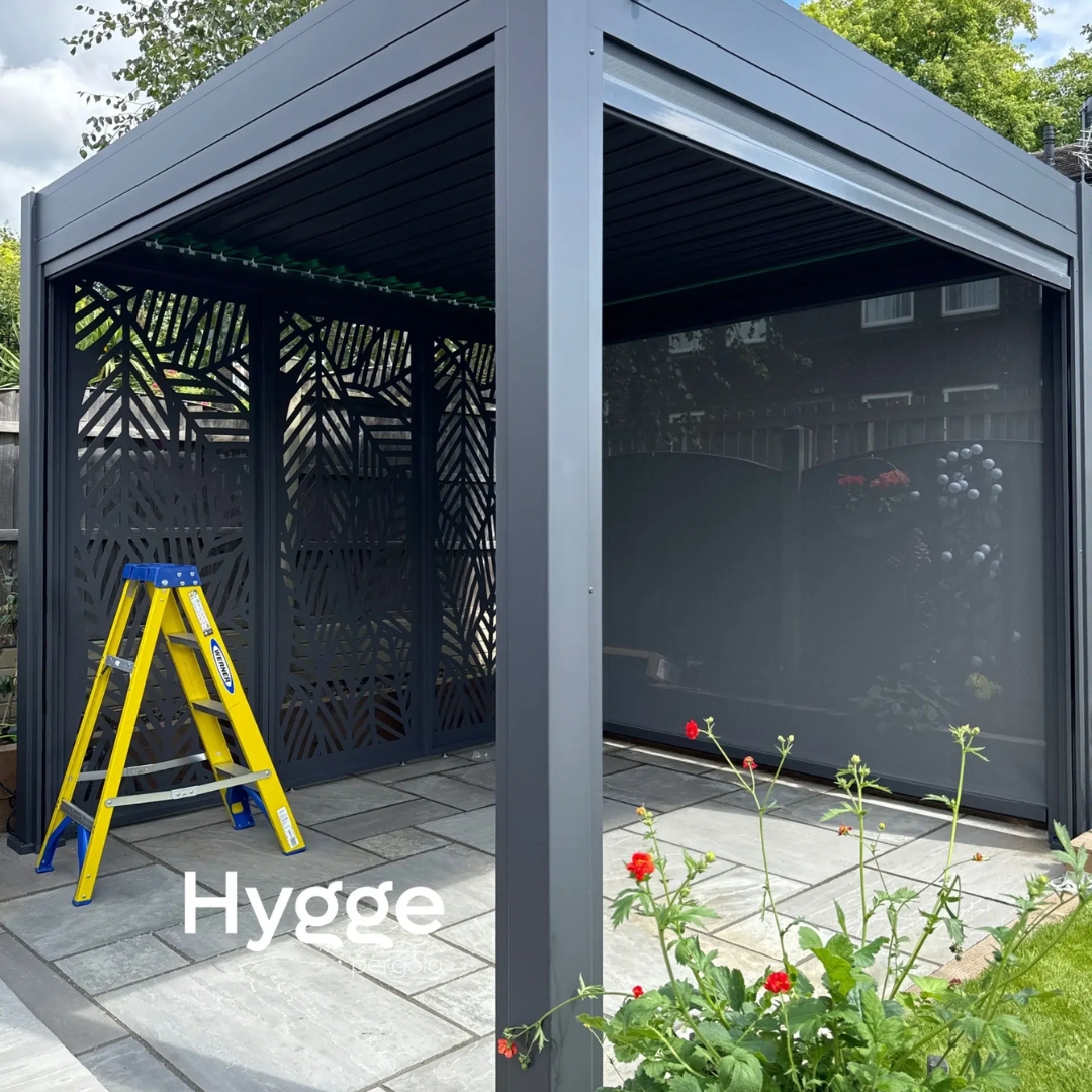 Luxury aluminium pergola with integrated lighting and closed side panels in a lush garden setting.