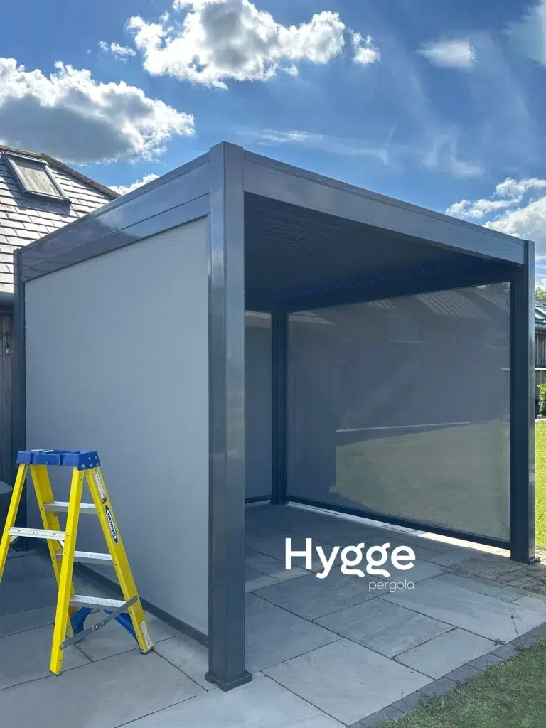 Dark grey aluminium pergola with an open louvred roof, providing adjustable shade in a garden setting.