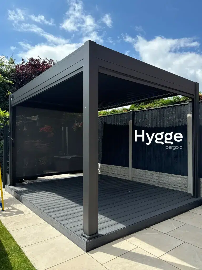 Modern dark grey aluminium pergola with slatted side panels, blending seamlessly into a garden space.